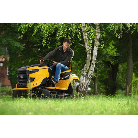 CubCadet 13AGA1TS603 lawn tractor in yellow, side view, mowing grass under trees outdoors.