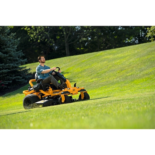 CubCadet 17AIGGY2603 zero-turn mower cutting grass on a sloped lawn, side angle outdoor photography