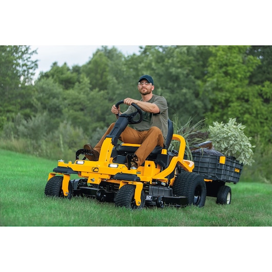 CubCadet 17AIGGY2603 yellow lawn mower towing trailer with plants, outdoor photography.
