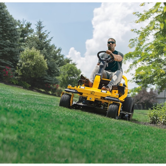 CubCadet 17AIGGY2603 yellow riding lawn mower mowing grass outdoors, front angle photography.