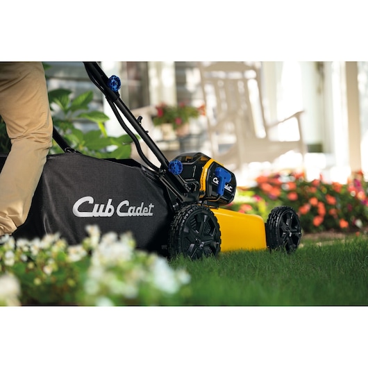 CubCadet 18ASTR94603 lawn mower side view with black grass bag and yellow body in a garden.