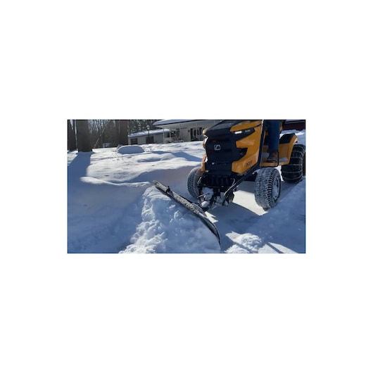 CubCadet 19A30017OEM snow plow attached to yellow lawn tractor clearing snow outdoors.
