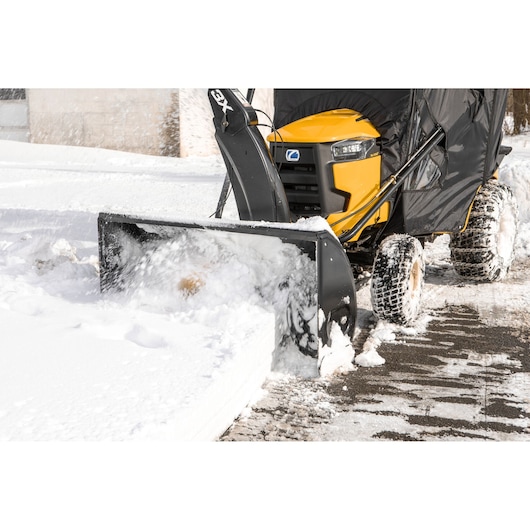 Photo of CubCadet 19A40024100 snow blower attachment on yellow tractor clearing snow, front angle.
