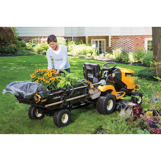 CubCadet 19A40030OEM garden cart attached to yellow lawn tractor, loaded with plants and tools, outdoor scene.