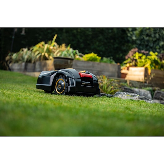 CubCadet 22AKHEFA603 robotic lawn mower on grass, side view, garden beds in the background.