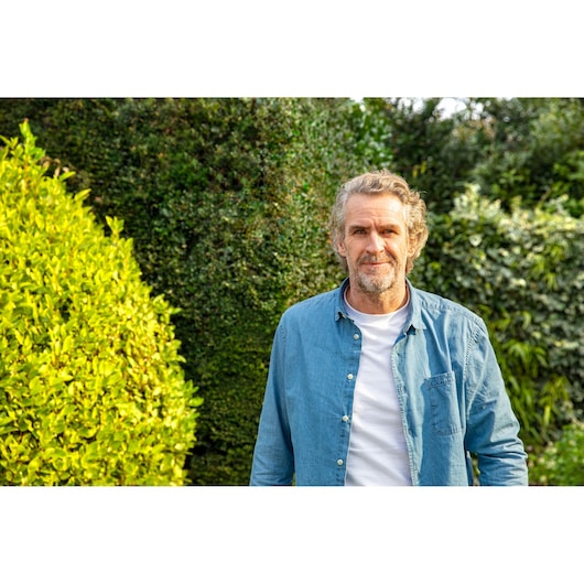 CubCadet 22AKHEFA603 photography of person in light blue shirt in garden with green hedges and yellow shrub.