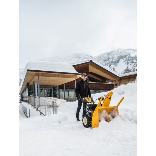 Photo of CubCadet 31AY5EVY603 yellow snow blower in use clearing snow outside a modern building.