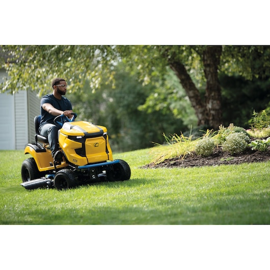 CubCadet 33ABA7ES603 yellow riding lawn mower in use on green grass near garden bed.