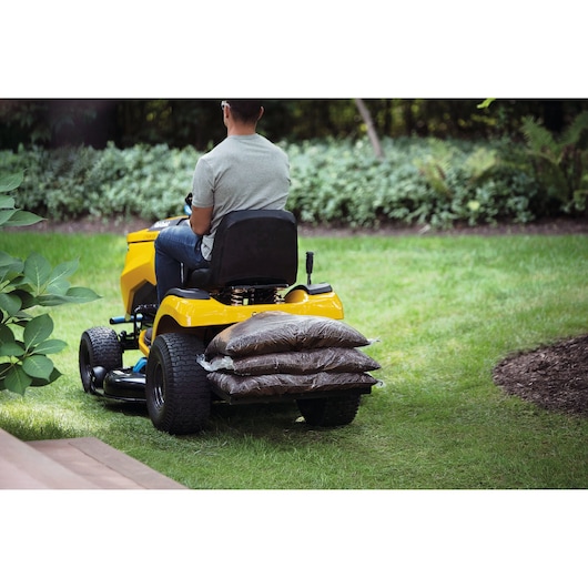 CubCadet 33ABA7ES603 yellow riding lawn mower carrying three mulch bags in a garden setting.