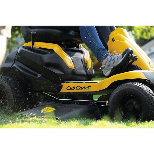 Photo of CubCadet 33BA27JD603 yellow ride-on mower cutting grass, side angle view showing wheels and deck.