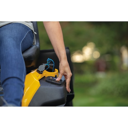 Person presses a control button on a yellow Cub Cadet outdoor equipment with close-up focus on hand and device.