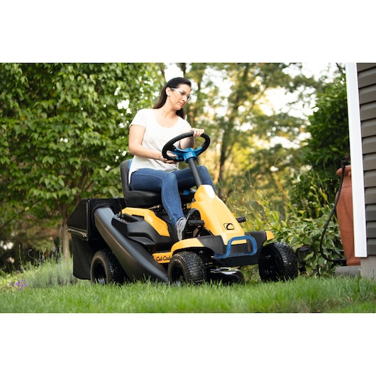 CubCadet 33BA27JD603 riding lawn mower with yellow body and black bagger, shown mowing grass outdoors.