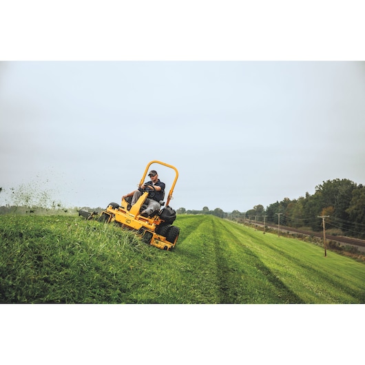 CubCadet 53ALHMUY603 stand-on mower cutting grass on a slope outdoors.